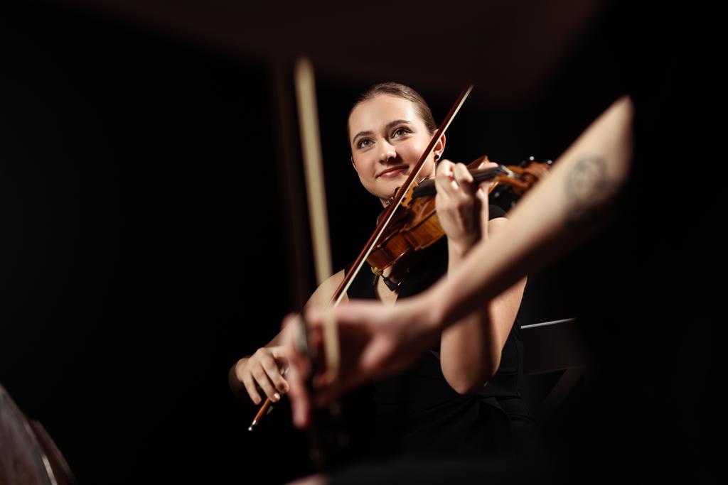 músicos profissionais sorridentes tocando música clássica em violinos no palco escuro
  - Foto, Imagem