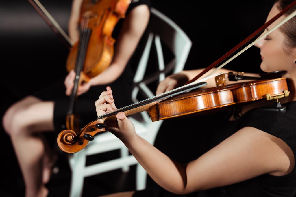 καλλιεργημένη άποψη των μουσικών που παίζουν βιολιά στη σκοτεινή σκηνή  - Φωτογραφία, εικόνα