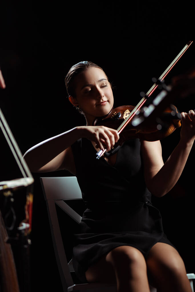 Ευτυχισμένη γυναίκα μουσικός με κλειστά μάτια που παίζει βιολί στη σκοτεινή σκηνή - Φωτογραφία, εικόνα