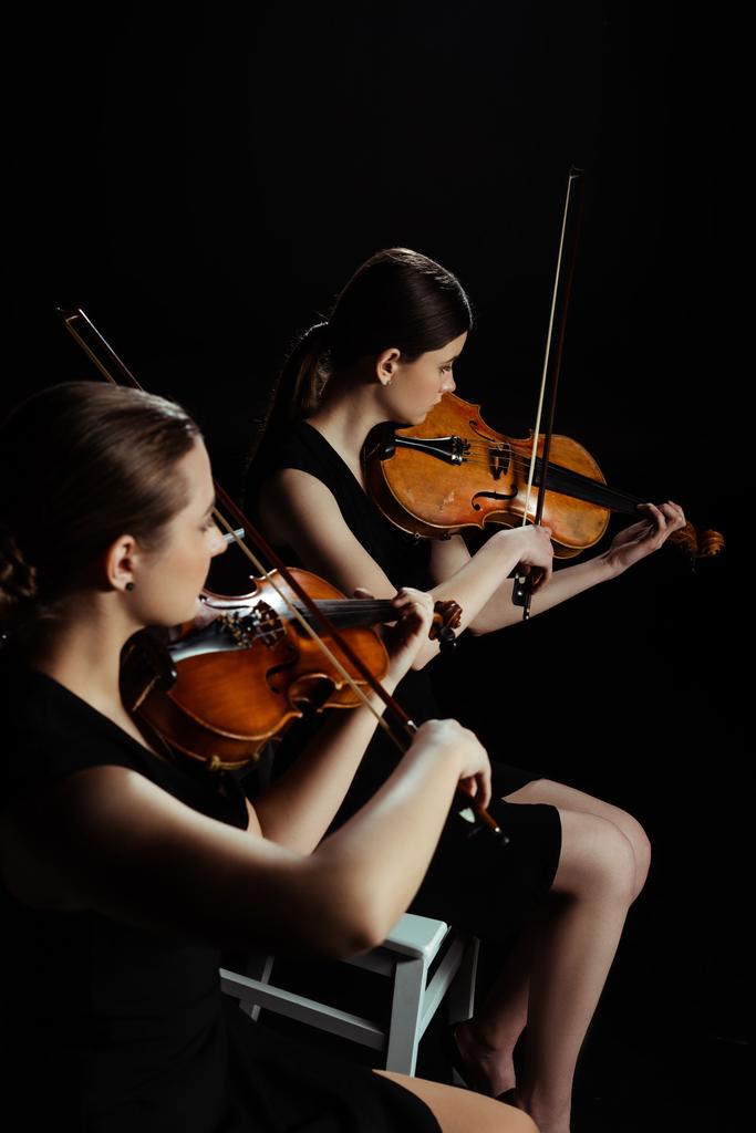 dois músicos profissionais tocando música clássica em violinos no palco escuro
  - Foto, Imagem