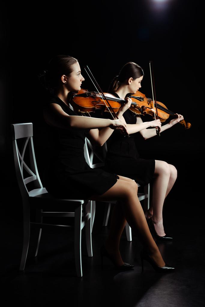 professional young musicians playing classical music on violins on dark stage  - Photo, Image
