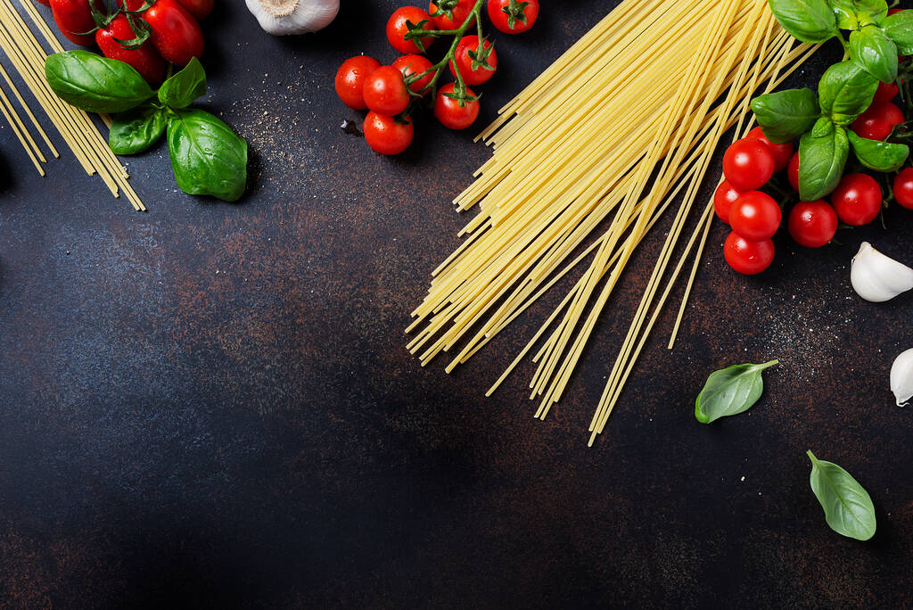 Ainesosat ruoanlaittoon italialaista pastaa: spagetti, tomaatti, basilika ja valkosipuli mustalla pöydällä. Top näkymä kuva kopioi tilaa
 - Valokuva, kuva