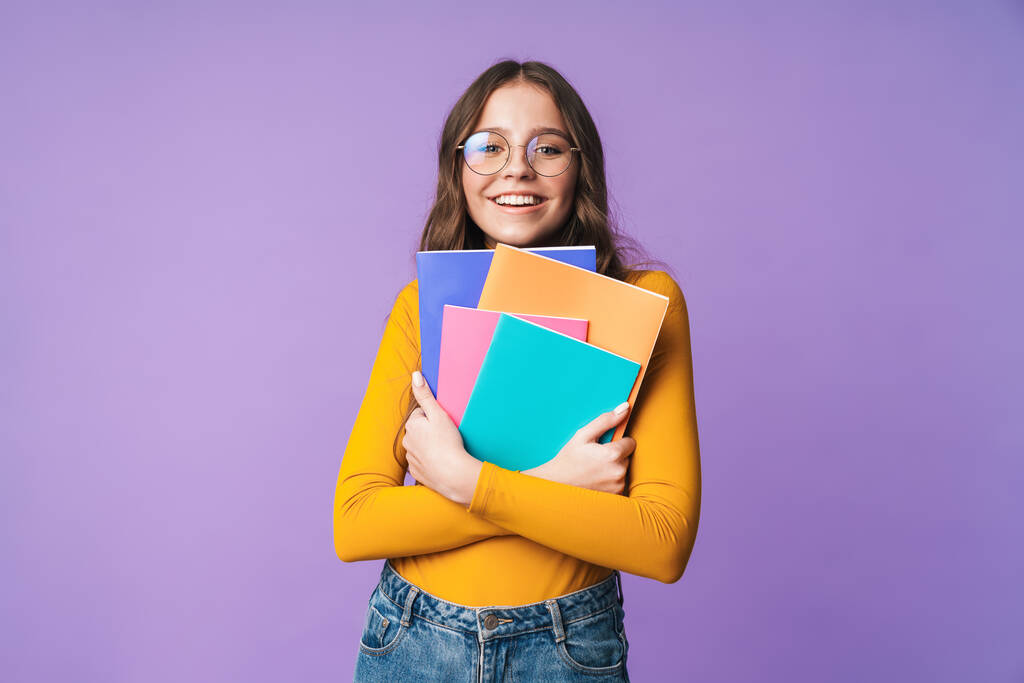 Image of young beautiful student girl wearing eyeglasses smiling and holding exercise books isolated over violet background - Photo, Image