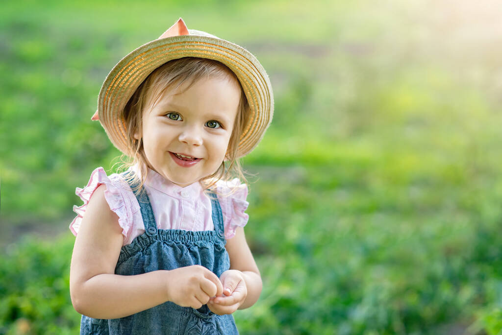 little farmer girl in hat eating pea pod in summer garden. Healthy eating for kid concept - Photo, Image