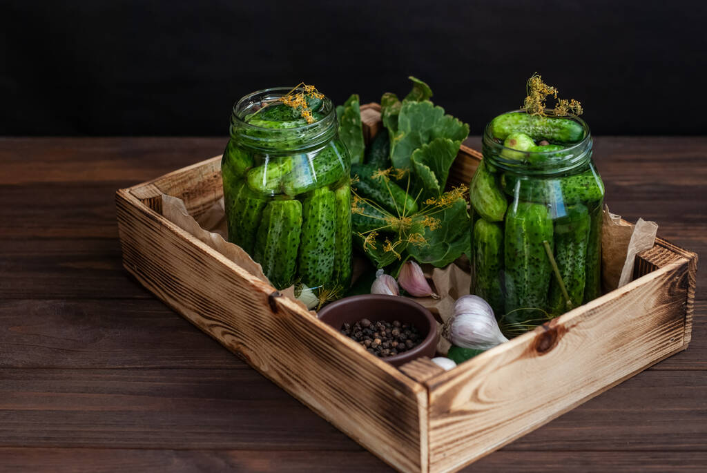 Fermentatie van komkommers in glazen potten. Rauwe komkommers, dille bloemen, kersenblad, mierikswortel blad, kruiden en specerijen op een dienblad, concept van biologische en gezonde voeding, augurken komkommers. - Foto, afbeelding