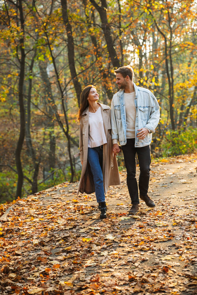 Full length of a beautiful young couple in love walking at the autumn park, holding hands - Photo, Image