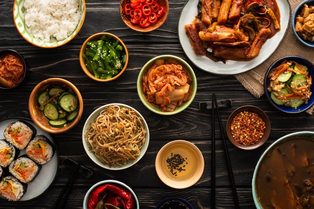 Draufsicht auf koreanische traditionelle Gerichte in der Nähe von Essstäbchen und Baumwollserviette auf Holzoberfläche  - Foto, Bild