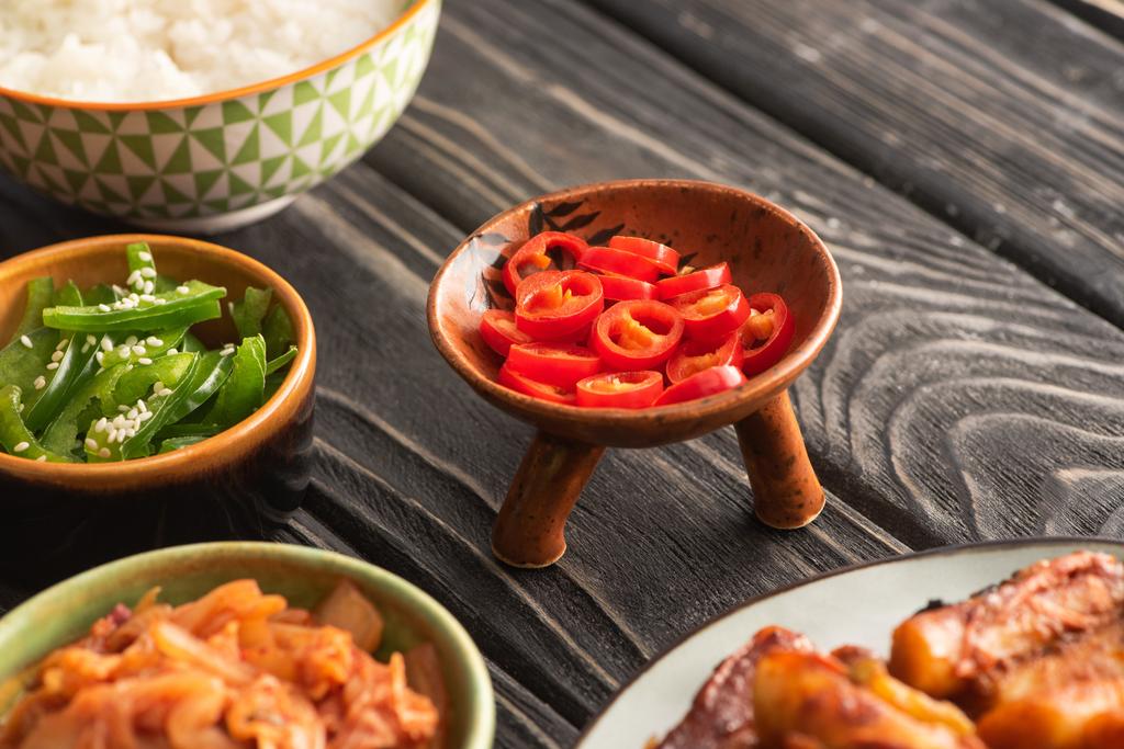 selektivní zaměření zelené papriky v blízkosti rýže, pikantní chilli papričky a korejské vedlejší pokrmy na dřevěném povrchu  - Fotografie, Obrázek