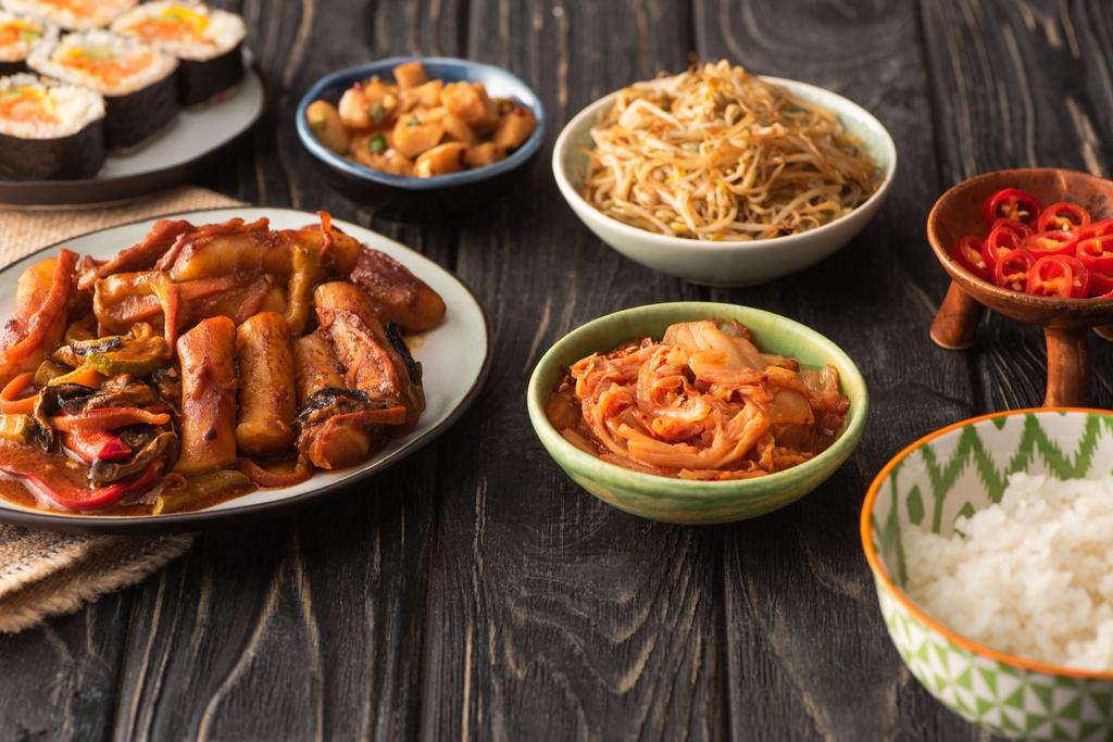 selektiver Fokus traditioneller Topokki in der Nähe schmackhafter koreanischer Gerichte auf Holzoberfläche  - Foto, Bild