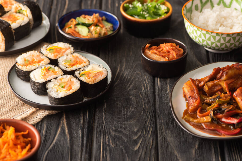 foco selectivo de gimbap tradicional cerca de sabrosos platos coreanos en la superficie de madera
  - Foto, Imagen