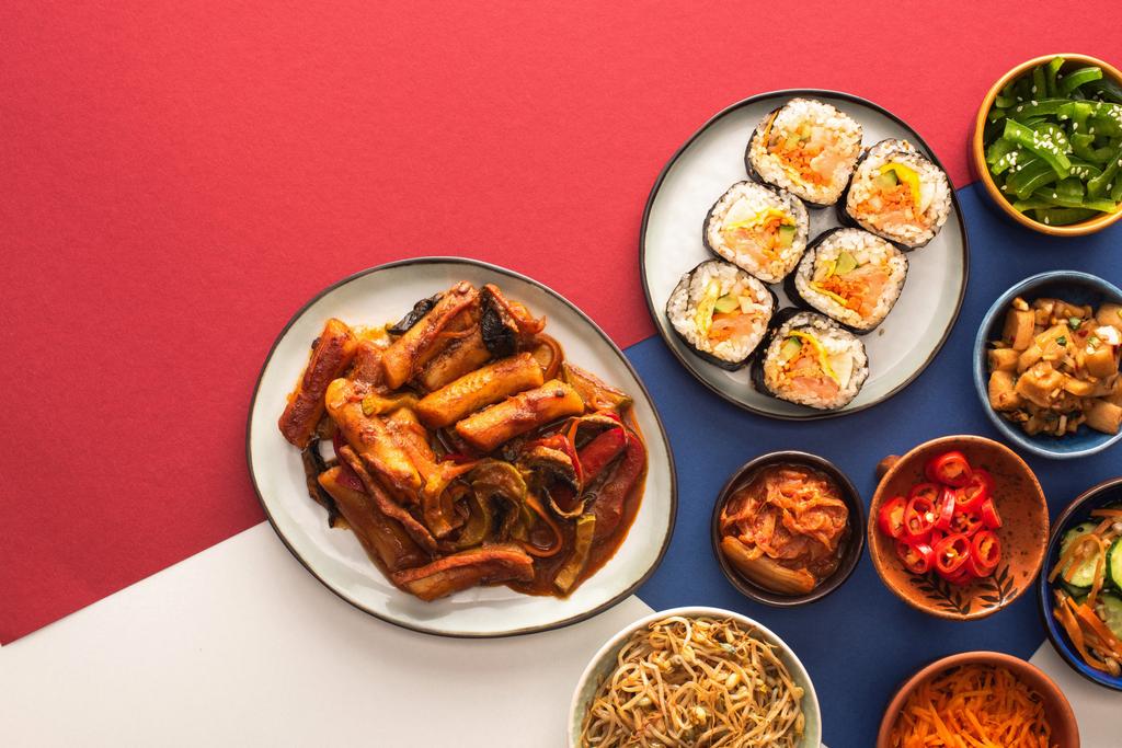 青くて真紅で白の辛い副菜の入った鉢のそばに韓国のトポッキが見える  - 写真・画像