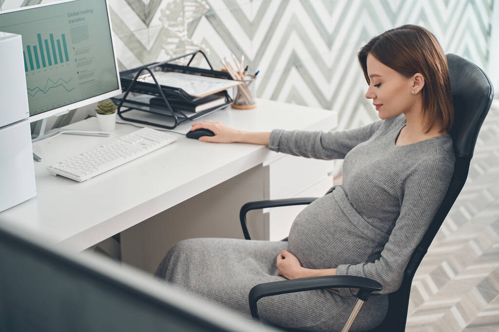 Sorridente donna incinta seduta a tavola al lavoro
 - Foto, immagini