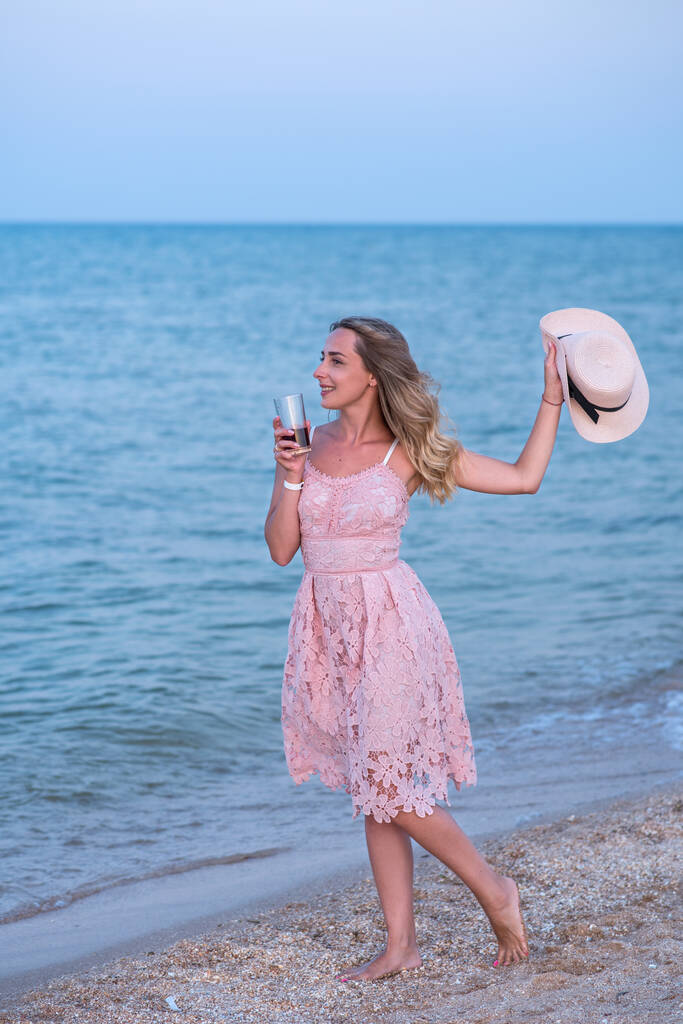 Tyttö, jolla on pallo rannalla. Nuori hattupäinen nainen rannalla. Nuori nainen vaaleanpunainen mekko rannalla. Lomat merellä
. - Valokuva, kuva