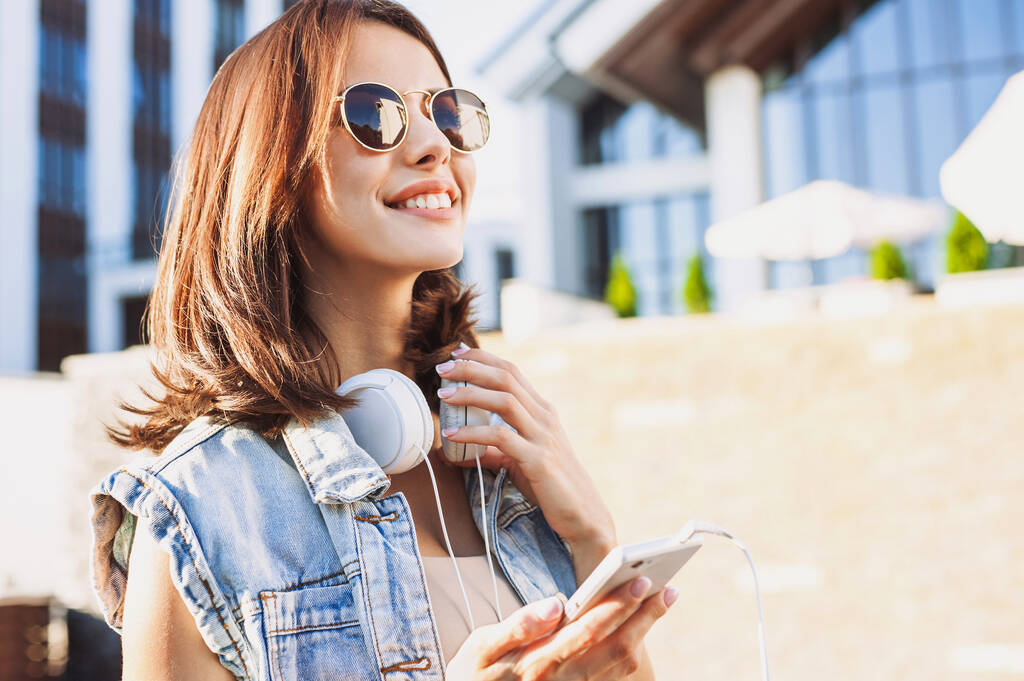 молода дівчина з навушниками, використовуючи смартфон на відкритому повітрі
 - Фото, зображення