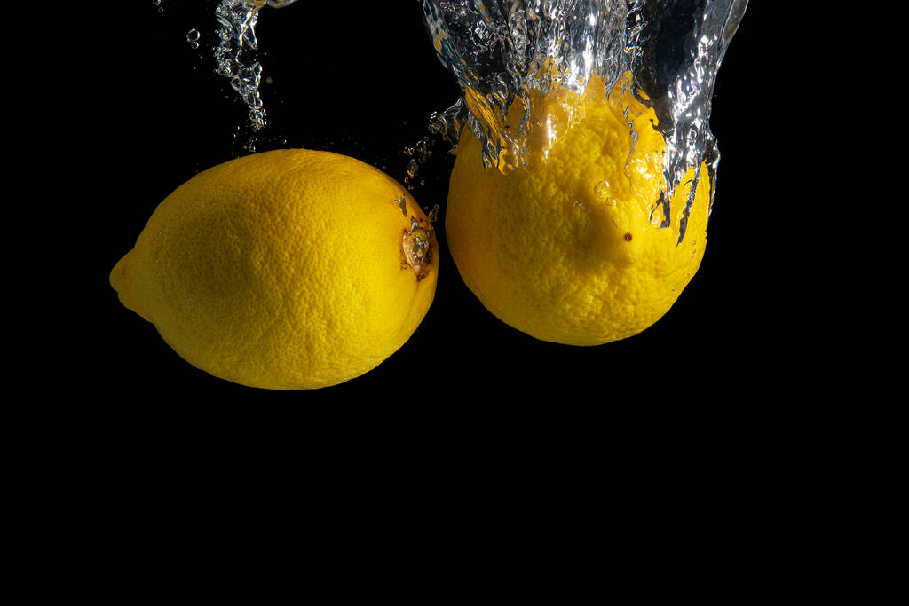 Frische gelbe Zitrone im Wasser spritzt isoliert auf schwarzem Hintergrund. Minimales Ernährungskonzept. - Foto, Bild