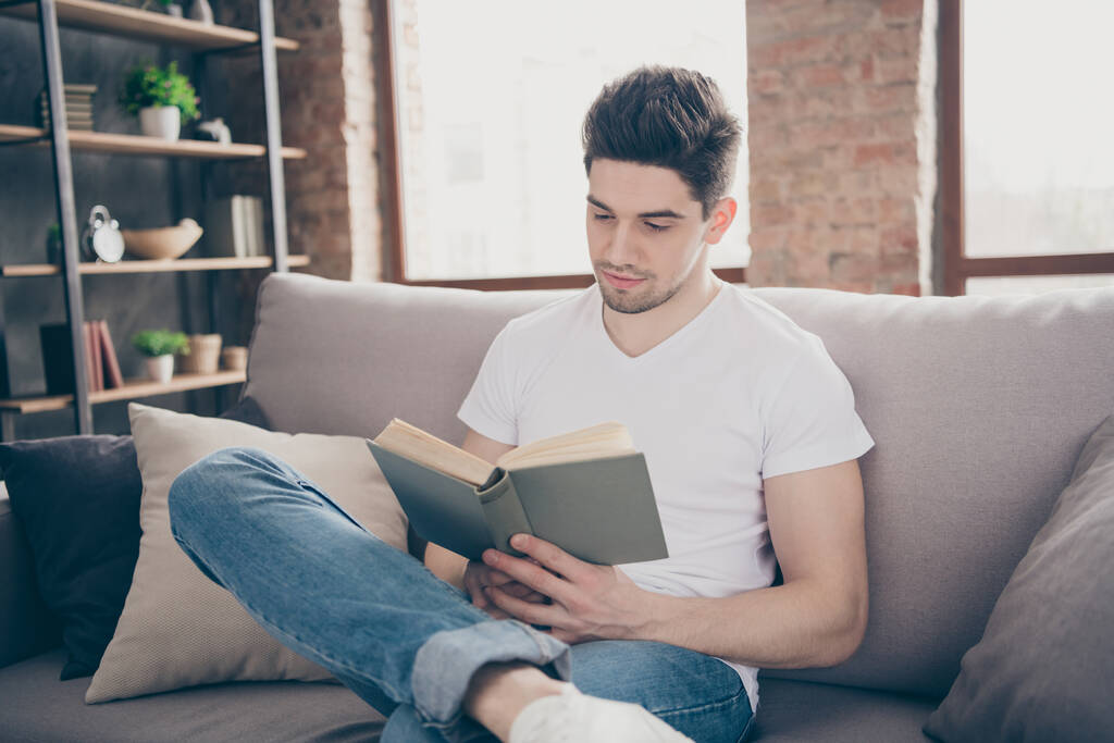 Portrait of his he nice attractive focused peaceful smart clever brunette guy sitting on divan reading paper book at modern industrial loft brick interior style living-room studio - Photo, Image