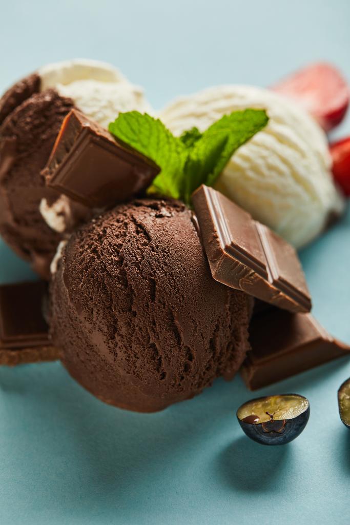 foco seletivo de sorvete marrom e branco saboroso com bagas, chocolate e hortelã em fundo azul
 - Foto, Imagem