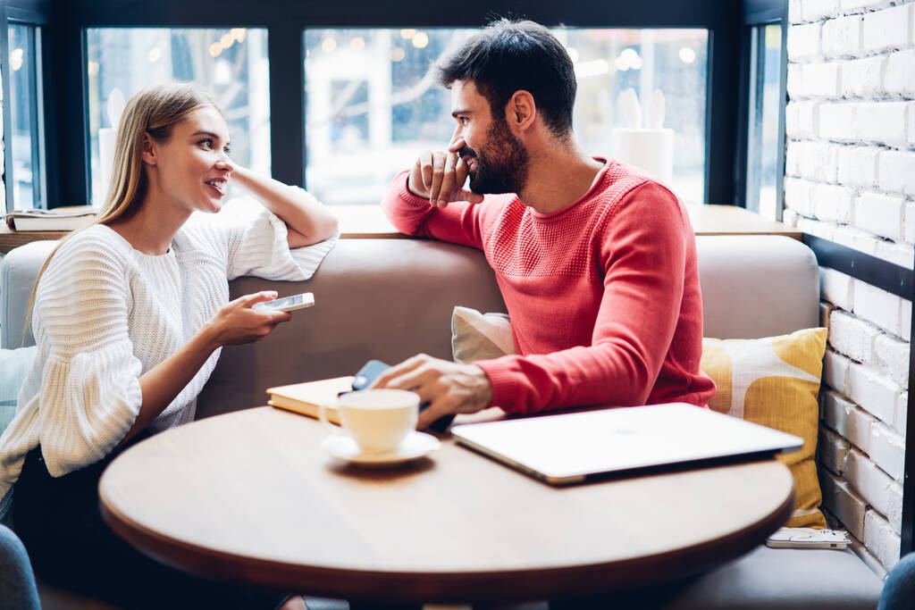 Positive couple in love sitting at cafeteria interior and discussing social networks addiction connecting to 4g wireless internet on modern devices, happy husband and wife spending leisure together - Photo, Image