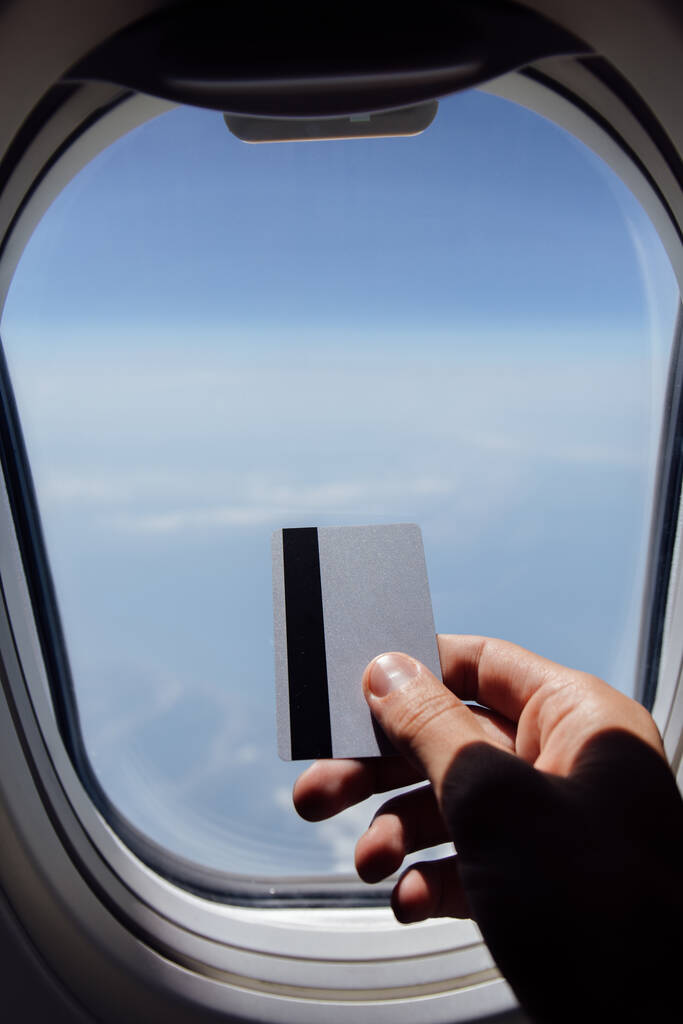 Περικοπή άποψη του ανθρώπου που κατέχουν πιστωτική κάρτα κοντά φινιστρίνι του αεροπλάνου  - Φωτογραφία, εικόνα
