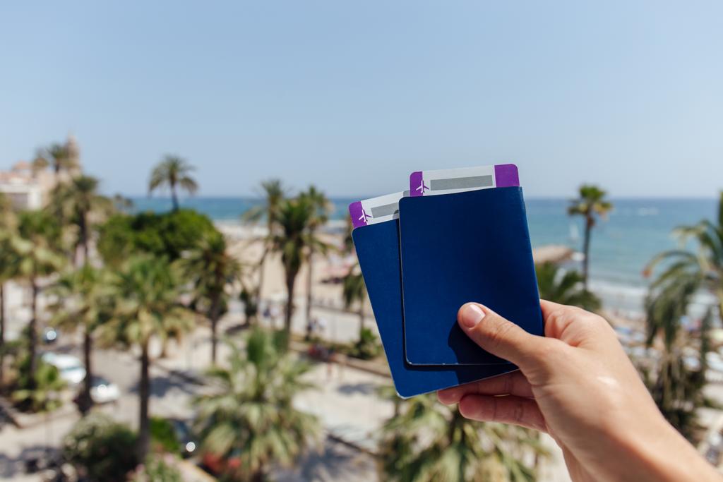 Vágott kilátás ember gazdaság útlevelek és repülőjegyek pálmafák és a tenger partján a háttérben - Fotó, kép