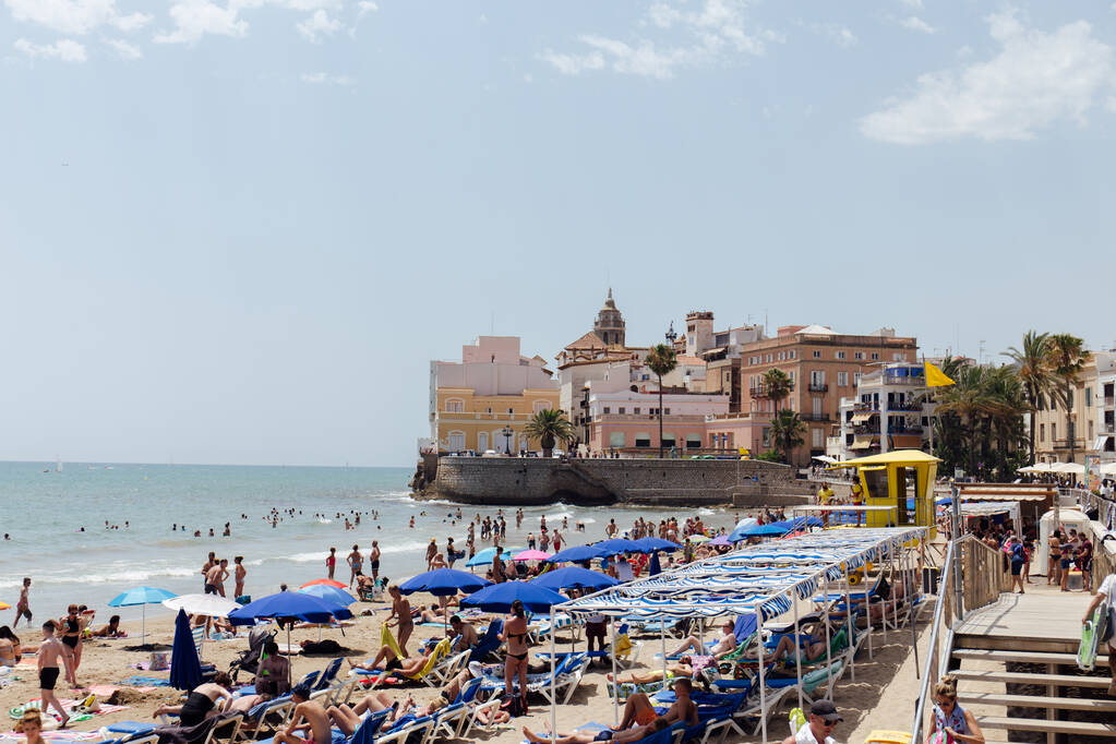 KATALONIEN, SPANIEN - 30. APRIL 2020: Menschen ruhen sich am Strand aus, mit Sonnenschirmen, Gebäuden und blauem Himmel im Hintergrund  - Foto, Bild