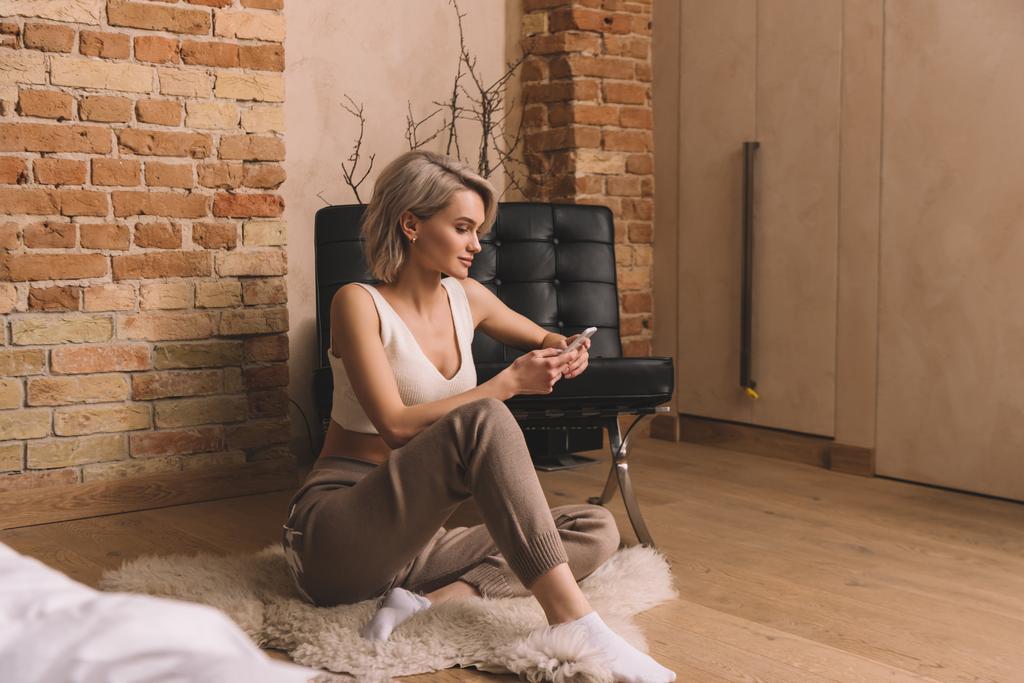 belle jeune femme assise de tapis hirsute et bavarder sur smartphone à la maison
 - Photo, image