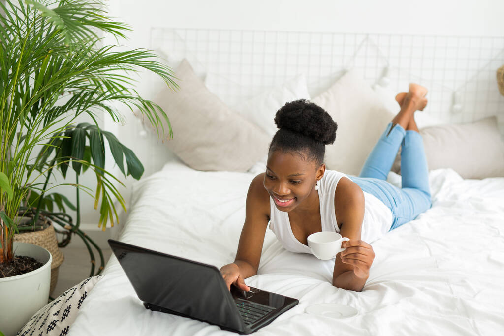 красива молода африканська жінка лежить на ліжку з ноутбуком
 - Фото, зображення
