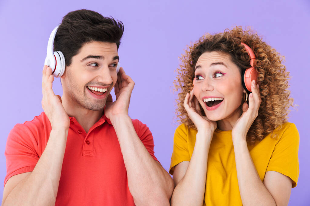 Portret zadowolonych osób rasy kaukaskiej mężczyzna i kobieta uśmiechnięci podczas słuchania muzyki wraz ze słuchawkami odizolowanymi na fioletowym tle - Zdjęcie, obraz