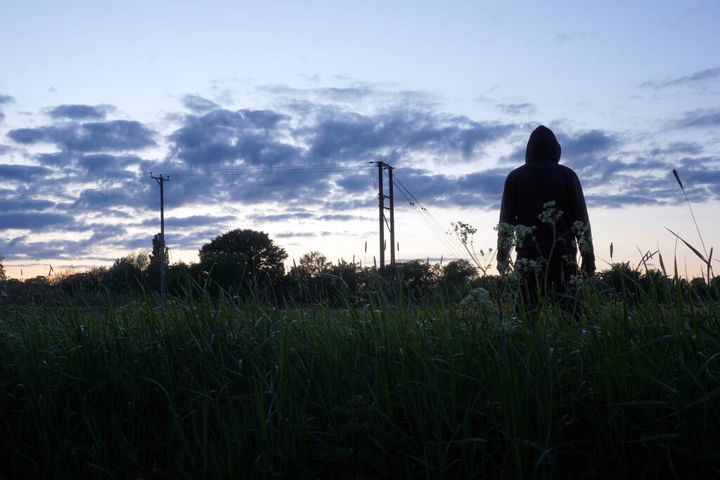 A mysterious hooded man looking at the sunset in a field of Buttercups. On a spring evening. - Photo, Image