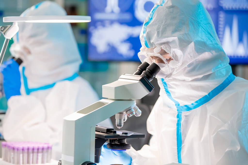 mikrobiolog badacz biotechnologii lub zespół pracowników medycznych wyglądają mikroskop w laboratorium z sukni izolacyjnej lub ochronnych garniturów i maski chirurgicznej twarzy - Zdjęcie, obraz