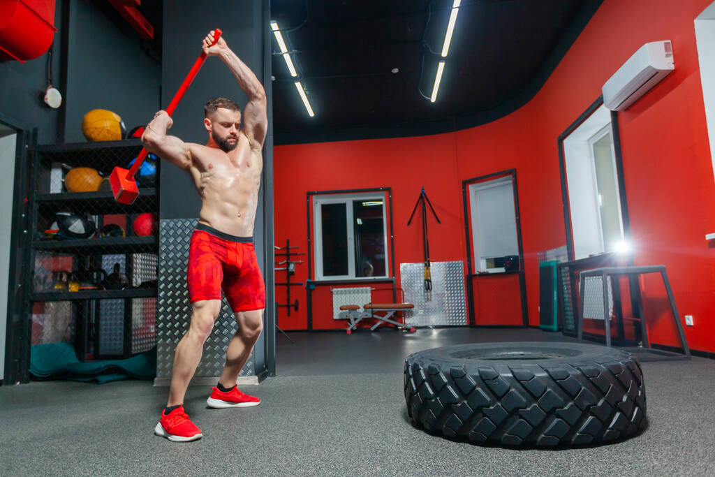 Retrato de comprimento total de homem musculoso forte realizando treino de marreta no ginásio moderno - Foto, Imagem