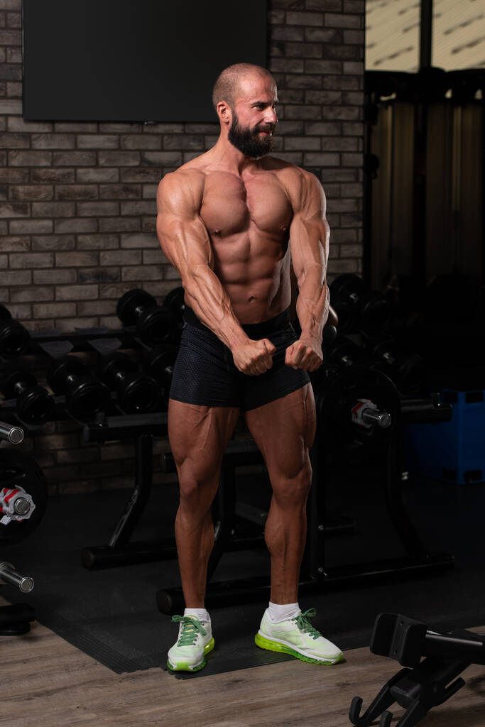 Красивый молодой человек, стоящий крепко в тренажерном зале и сгибая мышцы - мышечный атлетический культурист фитнес-модель позирует после упражнений - Фото, изображение