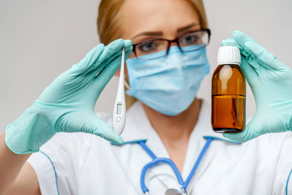 врач медсестра женщина в защитной маске и резиновых или латексных перчатках - держа банку лекарства и термометр
 - Фото, изображение
