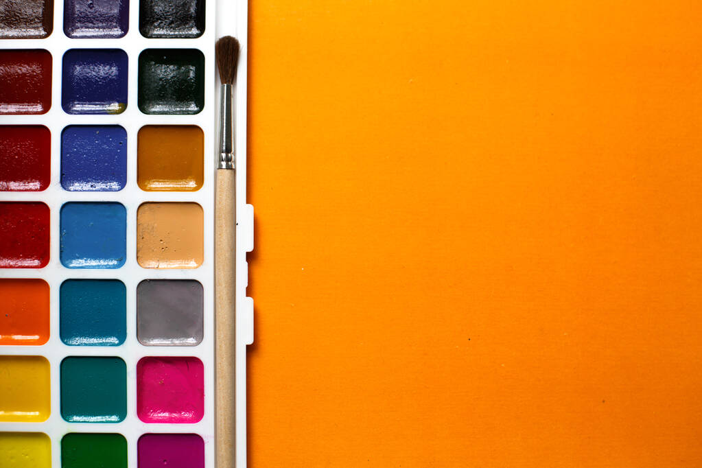 Eine Palette von Aquarellen und Pinseln auf orangefarbenem Hintergrund mit Platz für Text. Kreativ-Kurse mit Kindern zu Hause und in der Schule, Kunst-Meisterkurse, das Konzept der kreativen Entwicklung. - Foto, Bild