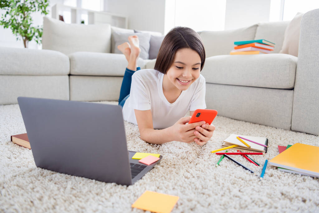 Photo of little pupil school lady chatting telephone classmates prepare notebook online lesson teacher lying floor near couch domestic social distance quarantine study comfort room indoors - Photo, Image