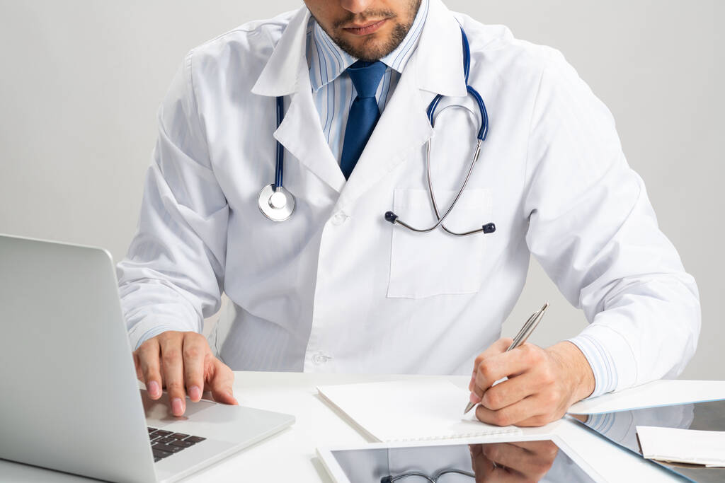 Successful therapist something writing at notepad. Physician in medical uniform with stethoscope working in office. Professional examination and diagnosis in modern clinic. Health care and treatment - Photo, Image