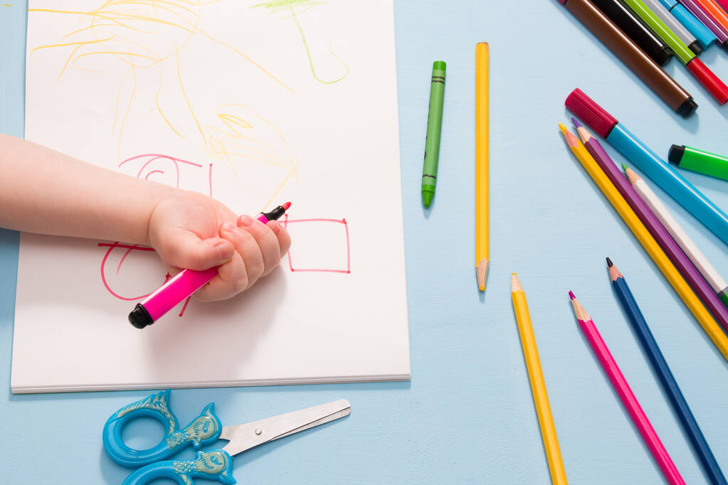 a small child painstakingly draws with a pink felt-tip pen in an album, copy space, top view, blue background, what to do with quarantine, activities for children at home - Photo, Image
