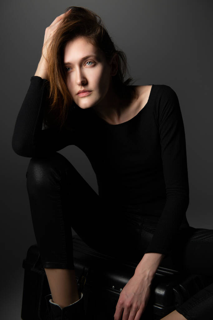 Modelo de moda. Mujer joven posando en estudio vestida de negro con botas. Hermosa chica caucásica sobre fondo gris - Foto, imagen