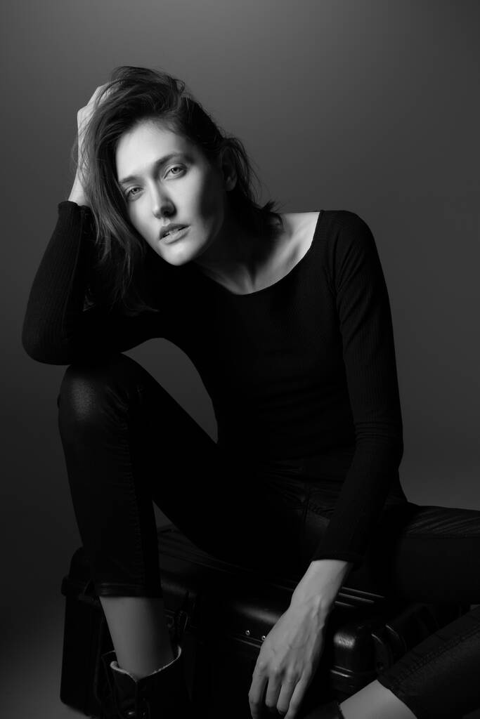 Modèle de mode. Jeune femme posant en studio portant du noir avec des bottes. Belle fille caucasienne sur fond gris. Noir et blanc - Photo, image