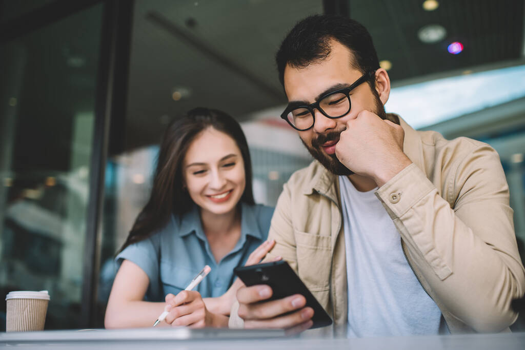 Šťastná žena sleduje vtipné video na mobilním telefonu asijského přítele tráví volný čas spolu v kavárně, hipster kluci kontrolují nes aktualizace pro aplikaci na smartphone přes 4G interne - Fotografie, Obrázek