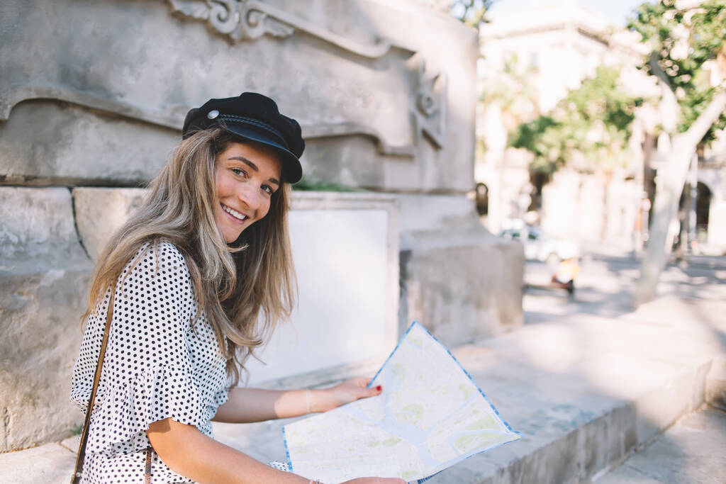 Ritratto di ragazza hipster positiva con berretto alla moda che sorride alla macchina fotografica mentre si riposa camminando ed esplorando la città di Barcellona per cercare un nuovo modo di mostrare sulla mappa cartacea, concetto di turismo
 - Foto, immagini