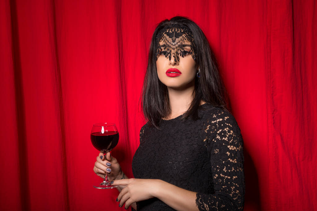 Mladá krásná žena drží sklenici vína přes červené závěsy - Fotografie, Obrázek
