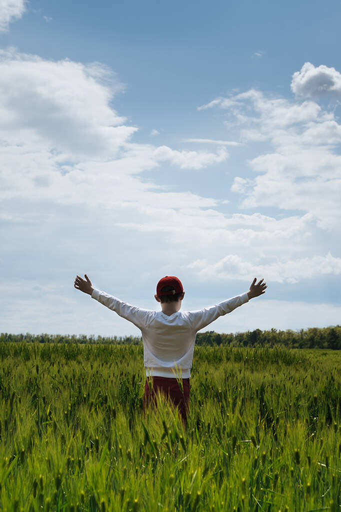 Un adolescente con le mani alzate in un campo di grano giovane
 - Foto, immagini