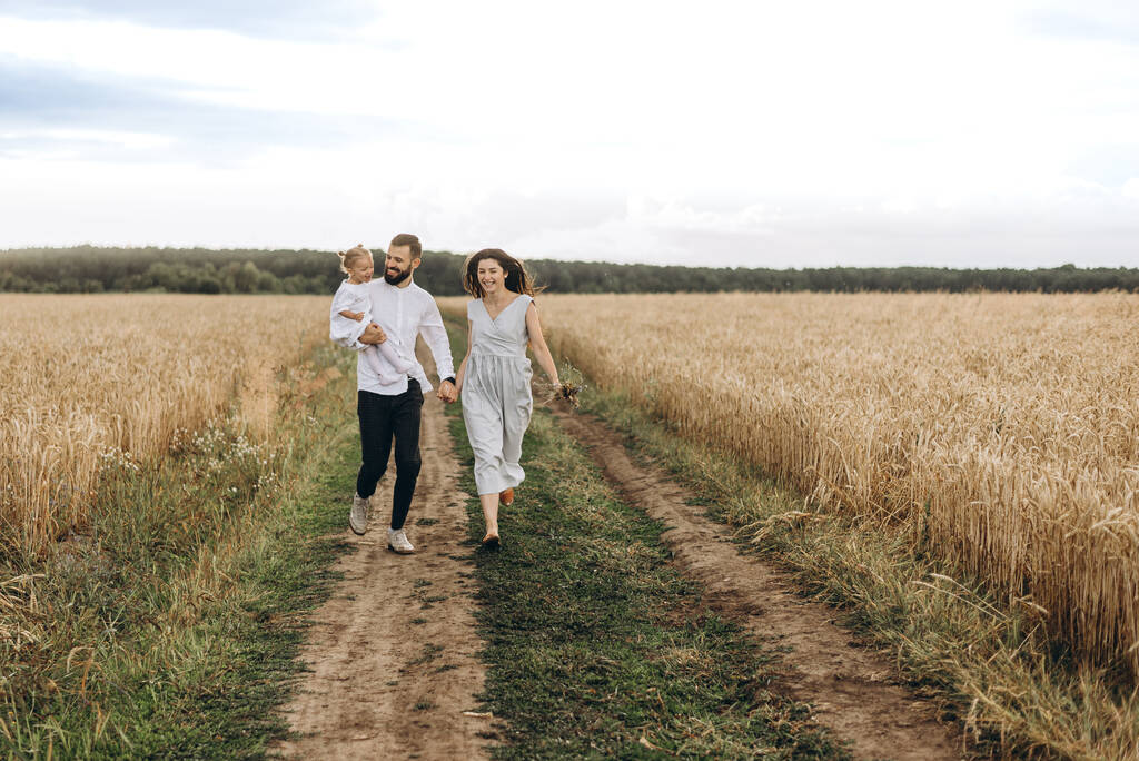 familia feliz en la caminata en el campo de trigo: Padre y una linda esposa joven con su hija pequeña padres felices con su bebé
 - Foto, Imagen