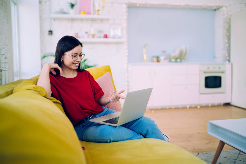 Happy casual kobieta chilling na kanapie w domu i rozmowy z przyjacielem za pośrednictwem laptopa na rozmowy wideo wskazując palcem na ekranie - Zdjęcie, obraz