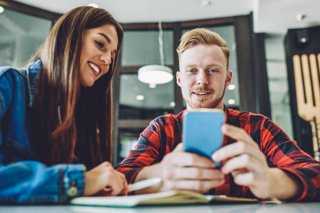 積極的な笑顔の男性と女性の学生は、広報分野で勉強から休憩を楽しみ、屋内無線4g接続を使用して通信のためのモバイルアプリケーションを介して友人とチャット - 写真・画像