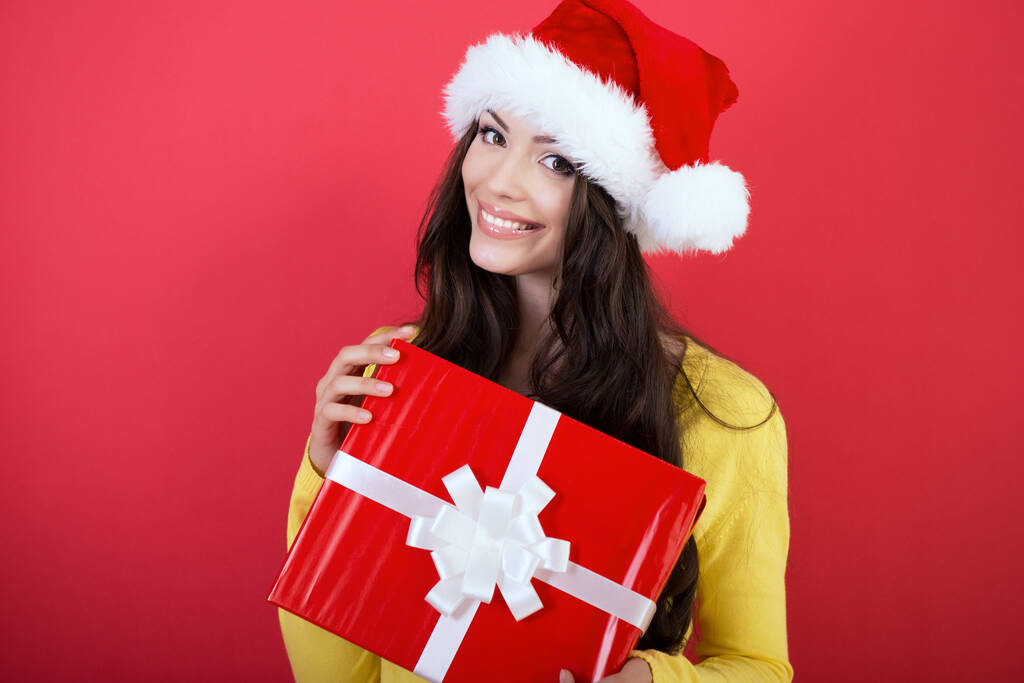 Kerstmeisje. Jonge mooie glimlachende vrouw met geschenkdoos, geïsoleerd op rode achtergrond, nieuwjaar en x-mas vakantie concept. - Foto, afbeelding