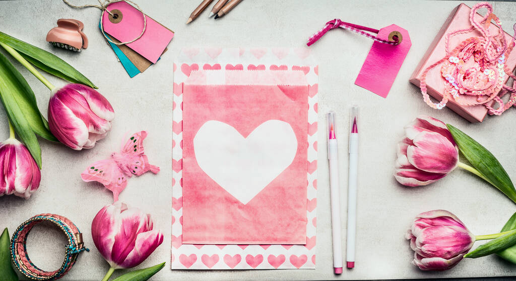 Kevät naisten työtila vaaleanpunainen tulppaanit kukkia, paperi kirjekuori sydän, harja merkit, tunnisteet ja lahjapaketti, ylhäältä näkymä, kopioi tilaa. Äitienpäivän lahja- ja onnittelukorttien teko
 - Valokuva, kuva