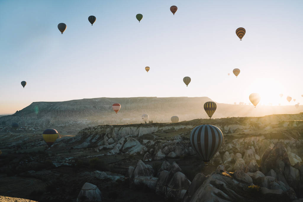 Vista aérea coloridos balões de ar quente em volta iluminado correndo uns aos outros ao amanhecer sobre terras altas e sol subindo no horizonte com céus claros - Foto, Imagem