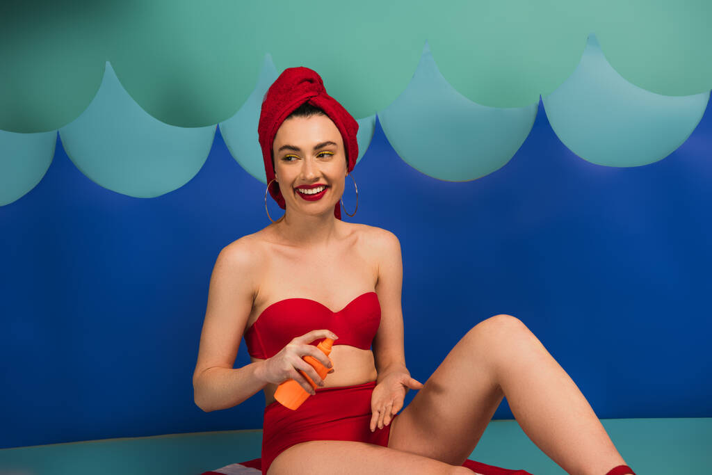 onnellinen nainen punaisella pyyhkeellä ja uimapuku soveltamalla aurinkovoidetta lähellä paperi leikata aaltoja
  - Valokuva, kuva
